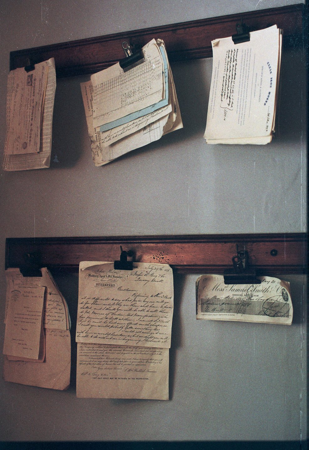 Documentos y cartas antiguas cuelgan de rieles de madera en una pared.